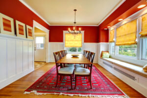 red persian rug in dining room being held down under the table to keep the rug from slipping around and causing any damage to the rug or to become a safety hazard in a room with a window and light hanging from the ceiling